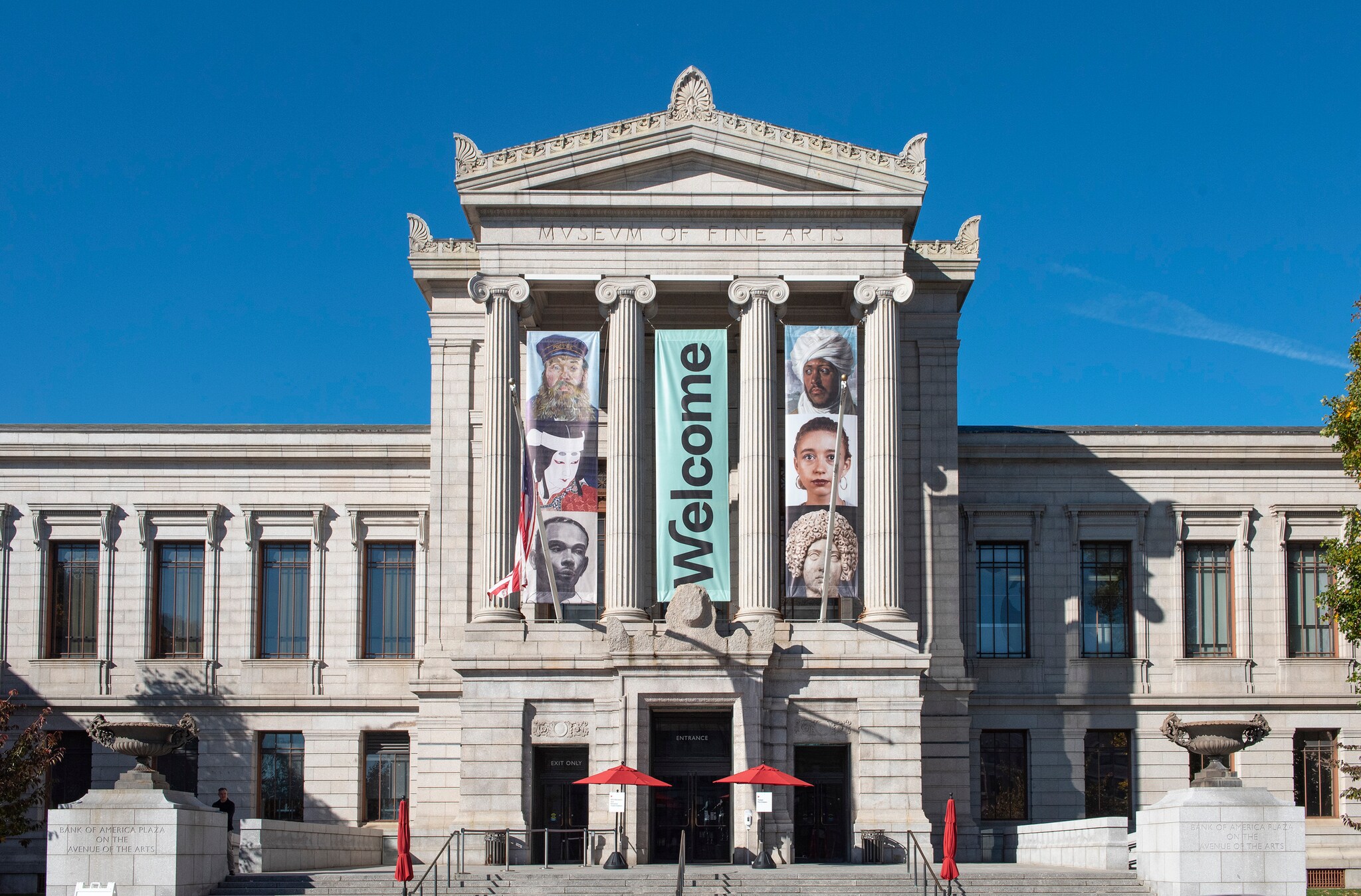 The Museum of Fine Arts, Boston, is a gray neoclassical building with banners displaying faces from global art and the word Welcome.