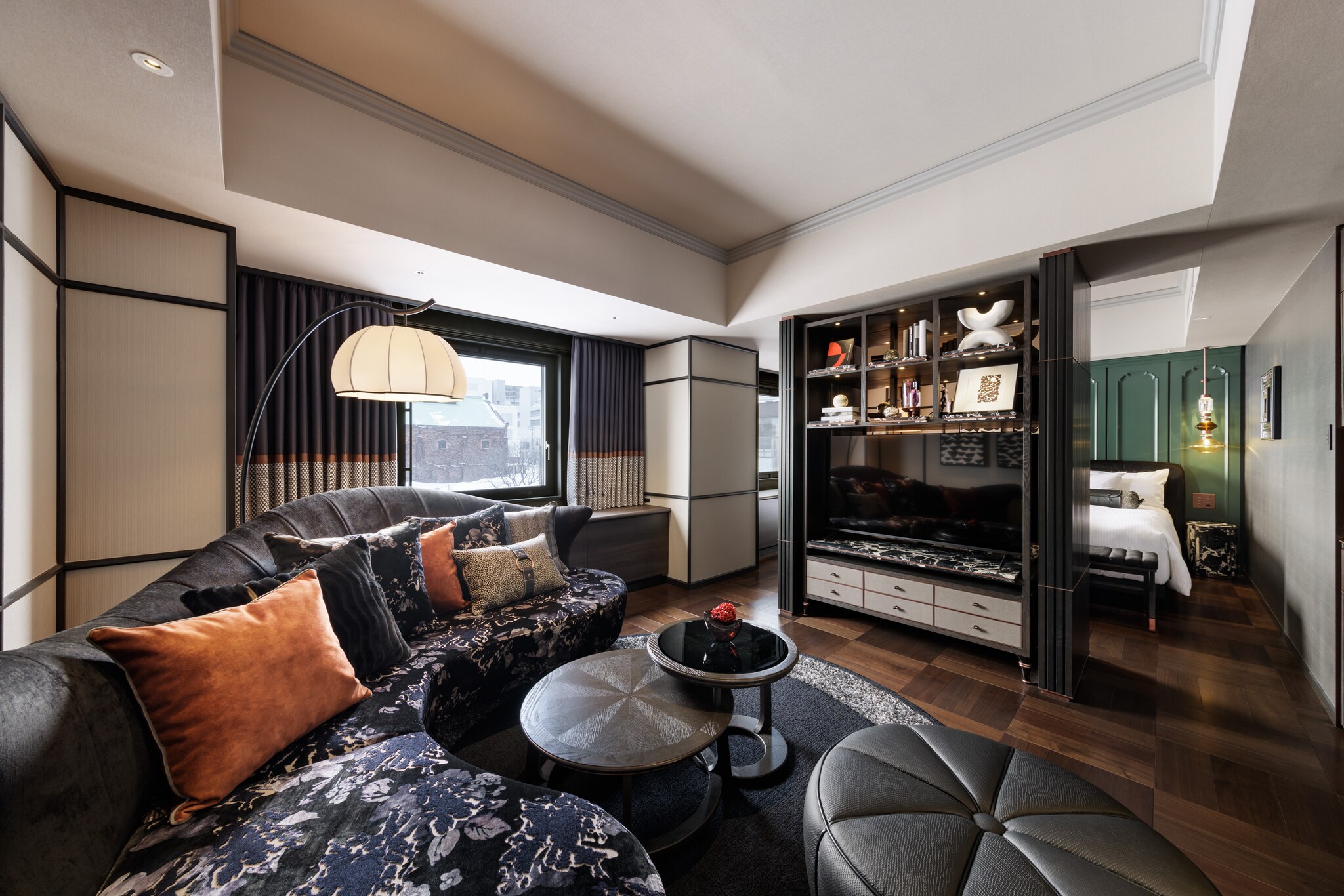 In the living area of the Hamanasu Suite, a curved, floral-patterned couch faces a sleek television. Beyond, the sleeping room is visible.
