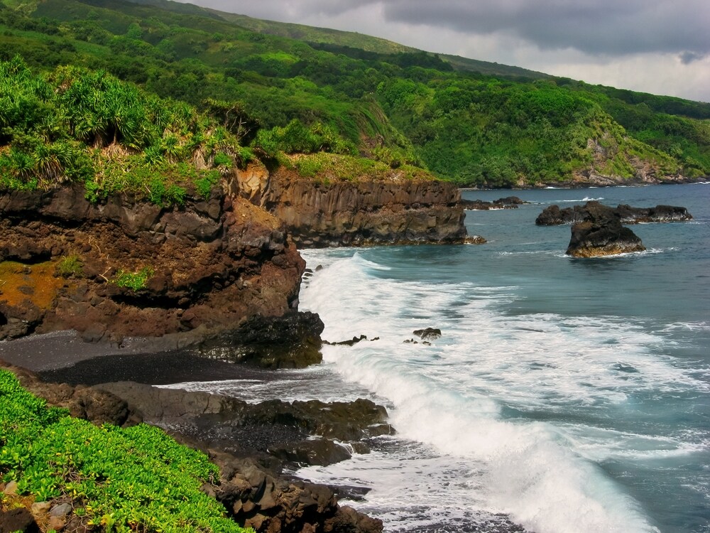 The ocean breaks on cliffs and volcanic rock covered in bright greenery.