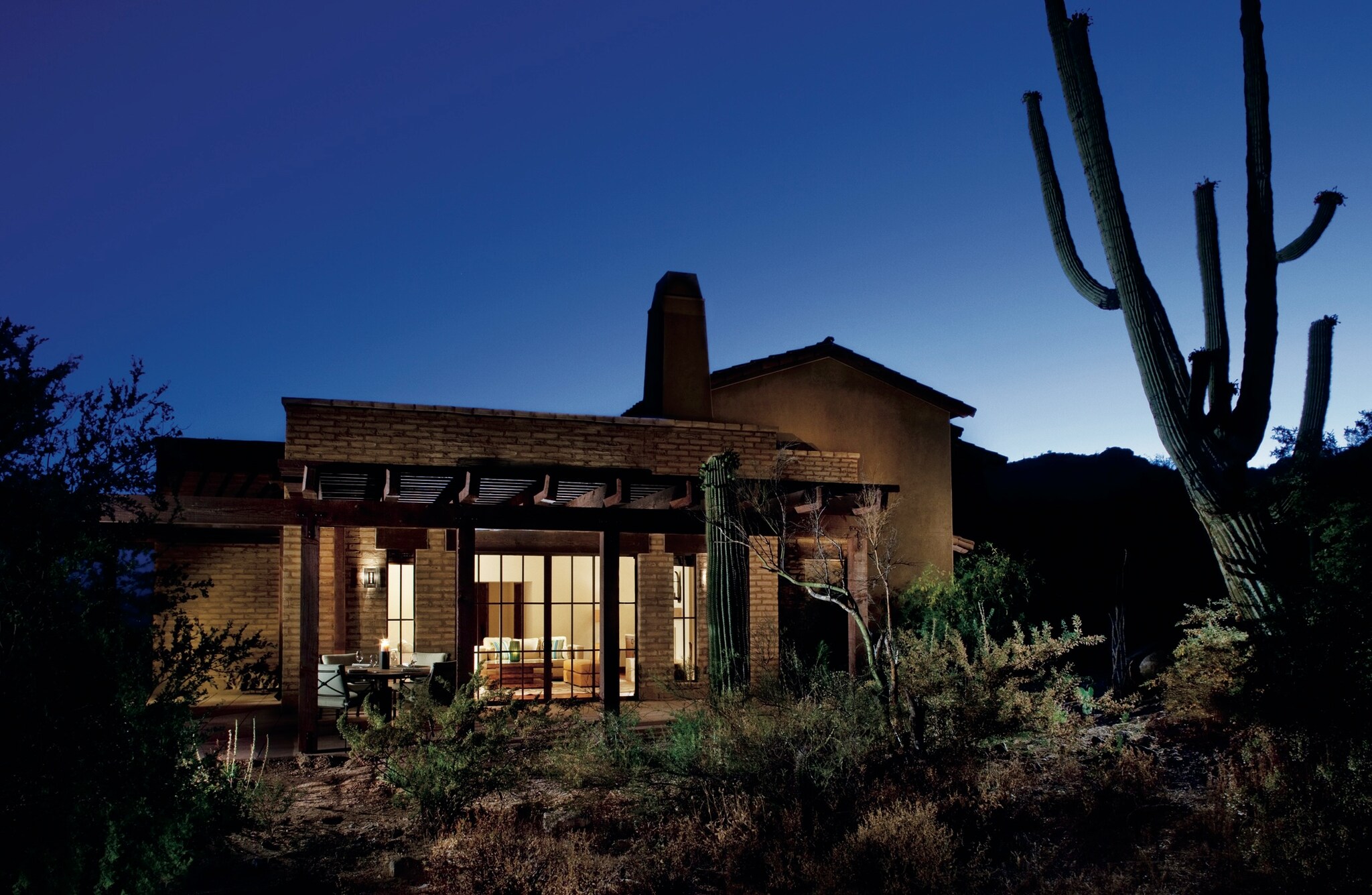 Early night view of a tan brick Casita Suite, with the low building and a cactus silhouetted against the last rays of sunlight.