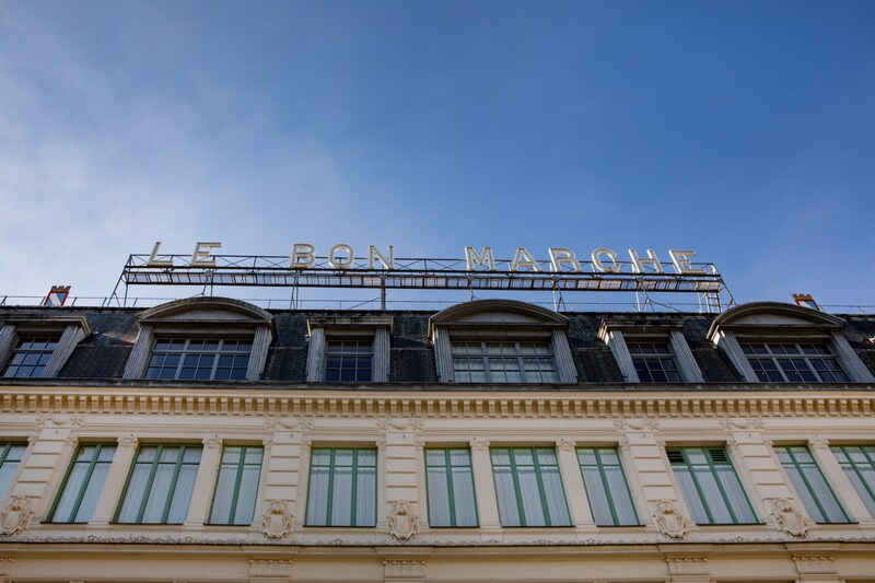 View up from in front of Le Bon Marché, the name of which is erected in huge letters atop its roof.