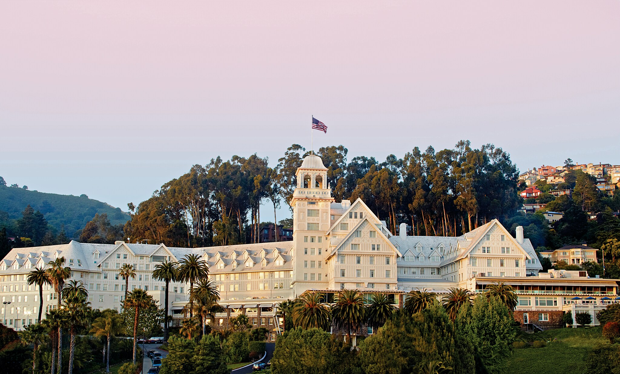 Exterior of the hotel at sunset. The sprawling white continental building is contrasted against palm trees near the top of a hill.