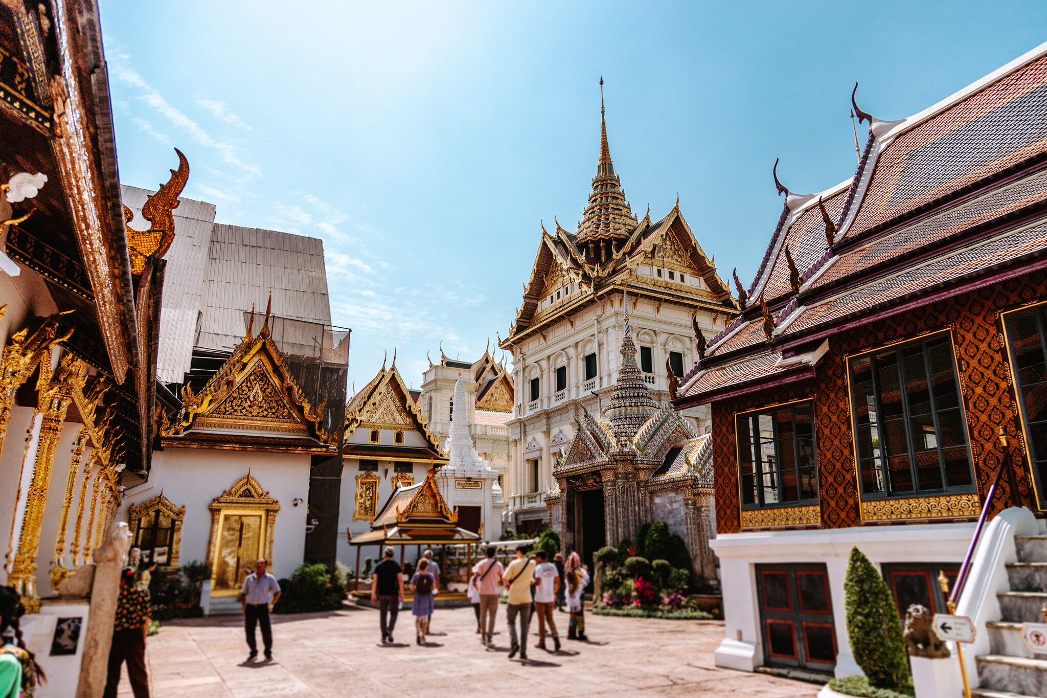Street-level view of the Grand Palace, the historic royal and parliamentary headquarters in Bangkok, with gilt, ornate panloms on the gables.