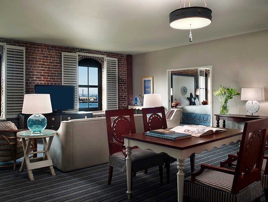A suite living room is eclectic with industrial and nautical accents, like a brick accent wall and a lamp with a glass buoy-like base.