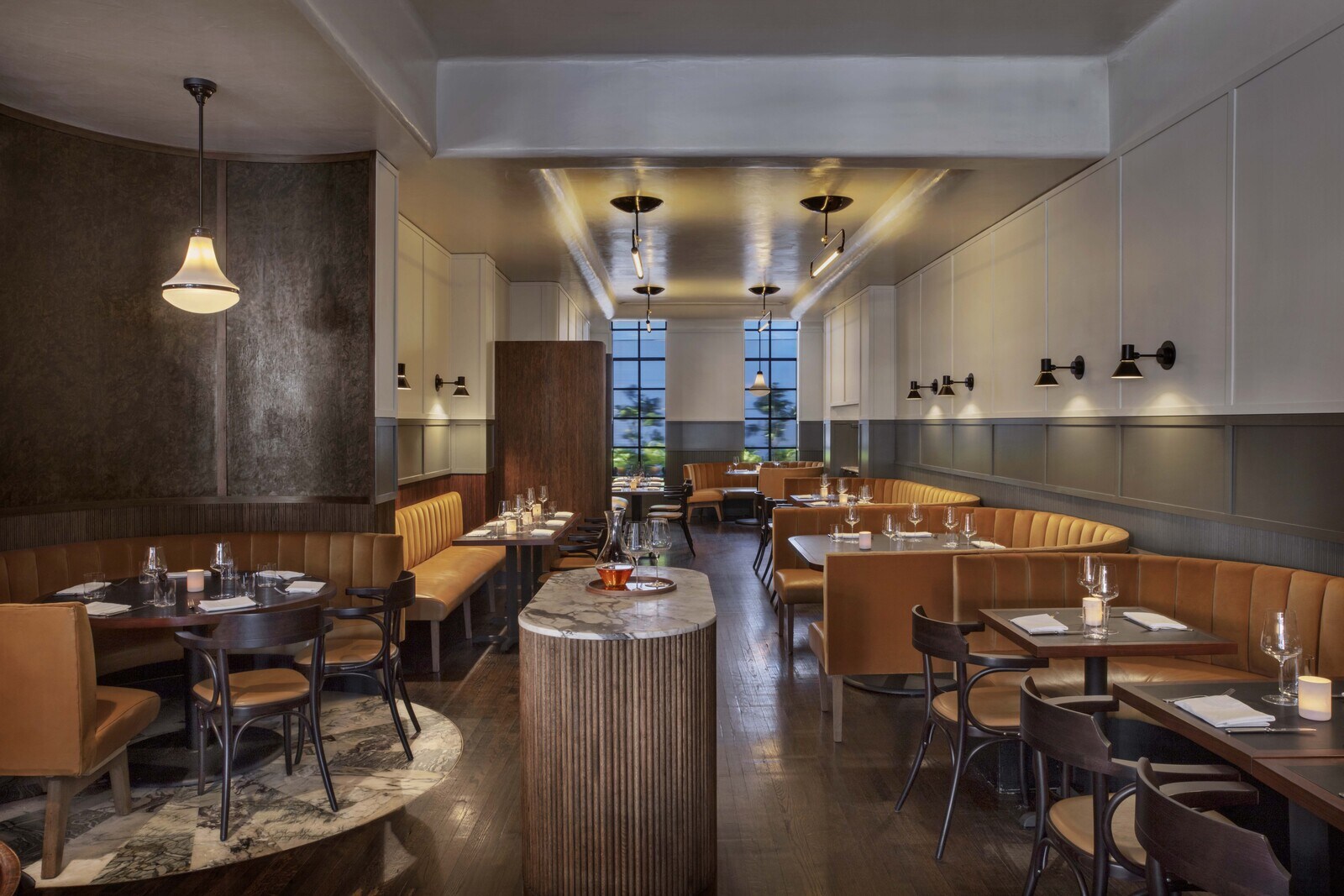 Inside The Noortwyck, curved tan leather booths alternate with small dining tables throughout a long dining room outfitted in neutral hues.