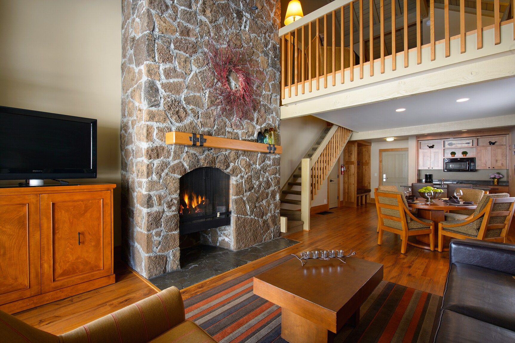 A stone fireplace warms the living area in a suite with a leather couch. A round dinner table is behind, with a lofted lounge area above.