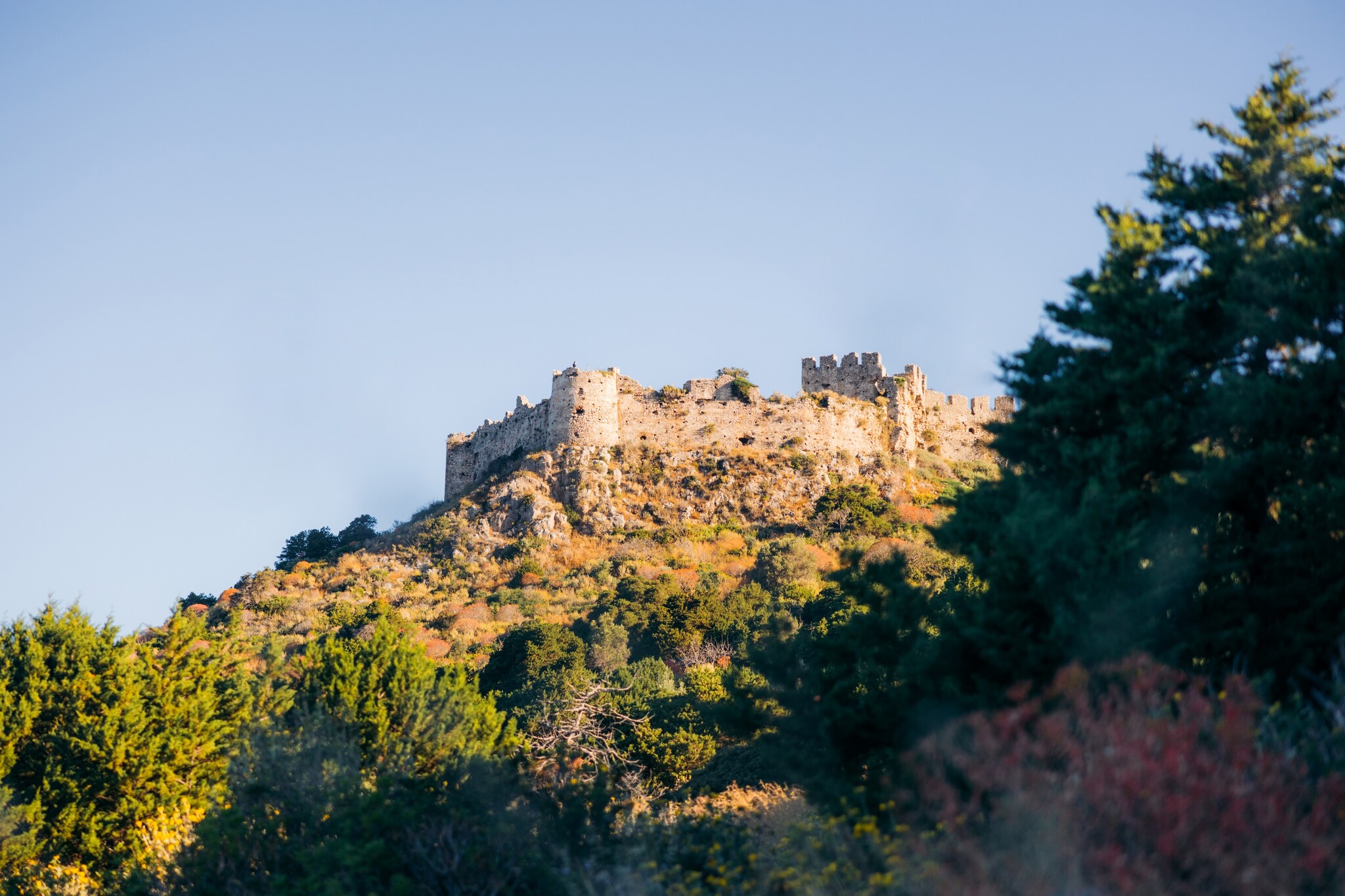 View up a scrubby hillside to a crumbling castle at its peak.