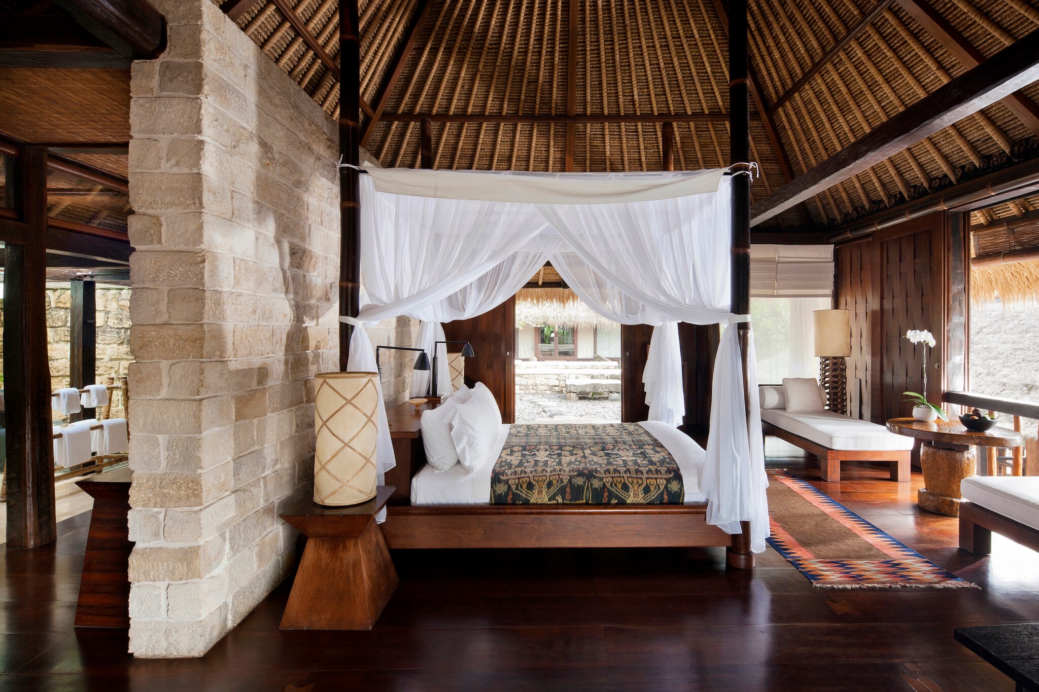 Terrace Suite Tejasuara has a brick wall dividing the bed from the rest of the room. A four-poster bed is draped with gauzy curtains.
