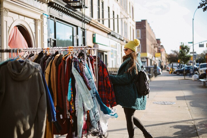 A white woman bundled up in warm clothes browses outdoor clothes racks on a New York City street.