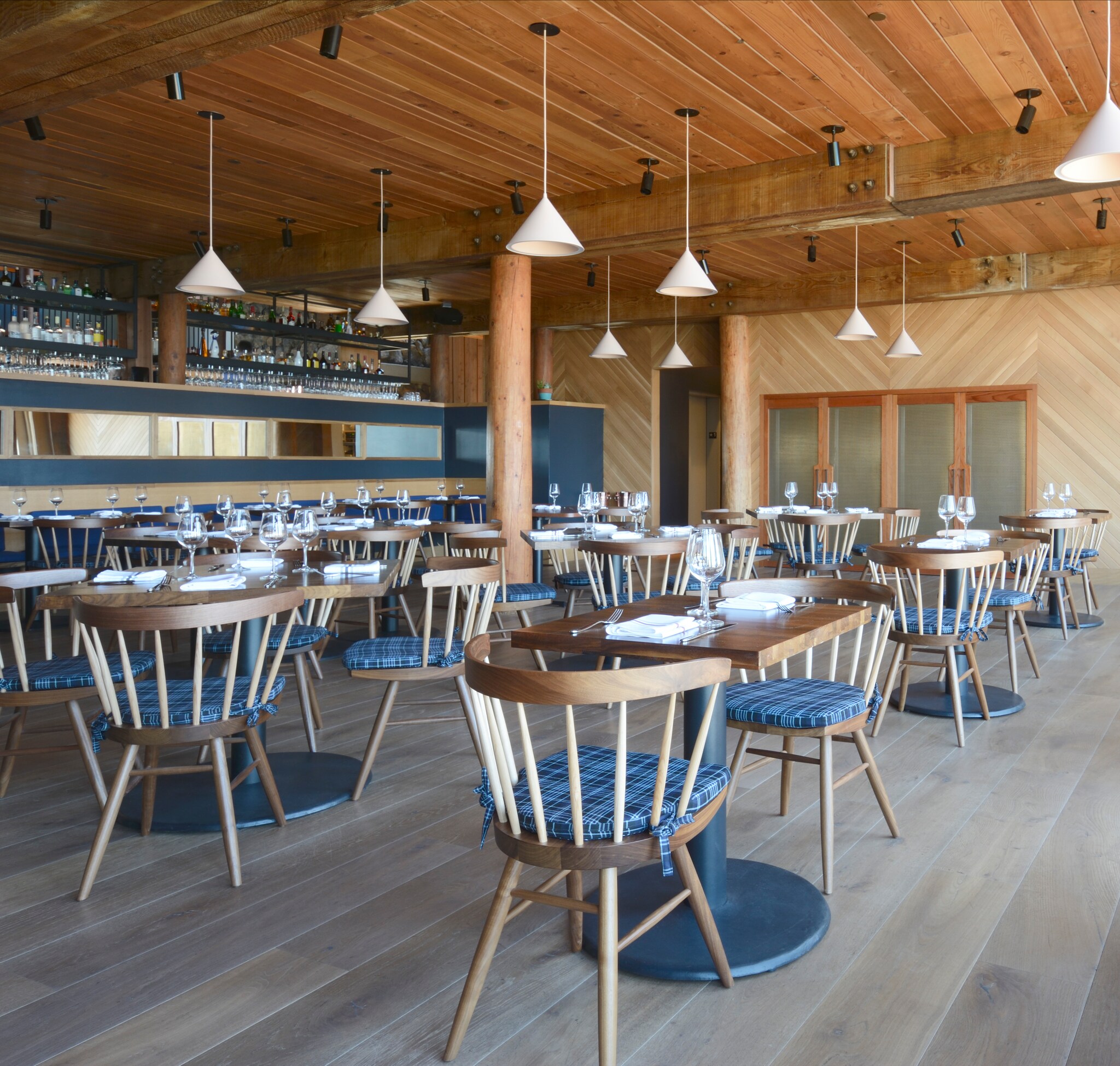 The tidy oceanfront dining room at Coast Kitchen has wood paneling on all walls, and plaid blue cushions on the wooden chairs.