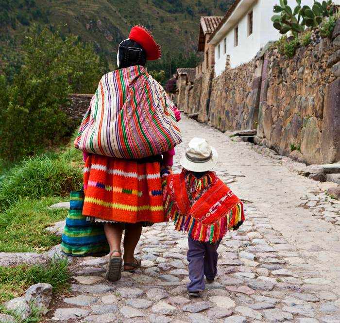 A woman and young child with their backs to the camera walk along a cobblestoned street wearing brightly patterned red clothes.