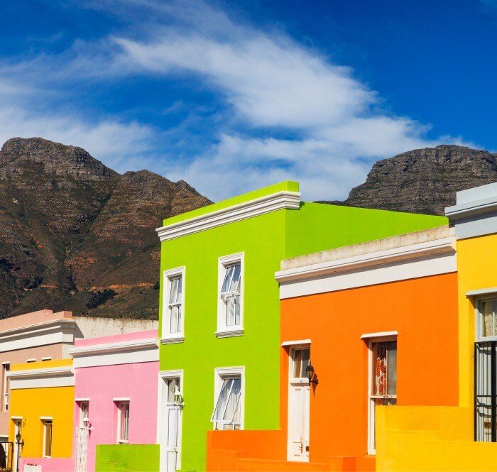A row of buildings painted in alternating bright colors—green, orange, pink, and yellow—contrast starkly with the rugged mountains behind.