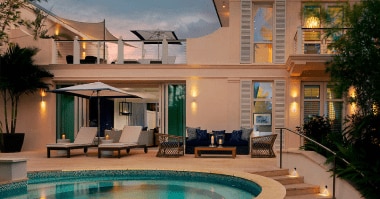 Exterior of a cream-colored, two-story villa at Rosewood Baha Mar. The veranda features seating and loungers next to a private plunge pool.