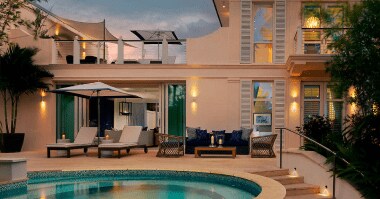 Exterior of a cream-colored, two-story villa at Rosewood Baha Mar. The veranda features seating and loungers next to a private plunge pool.