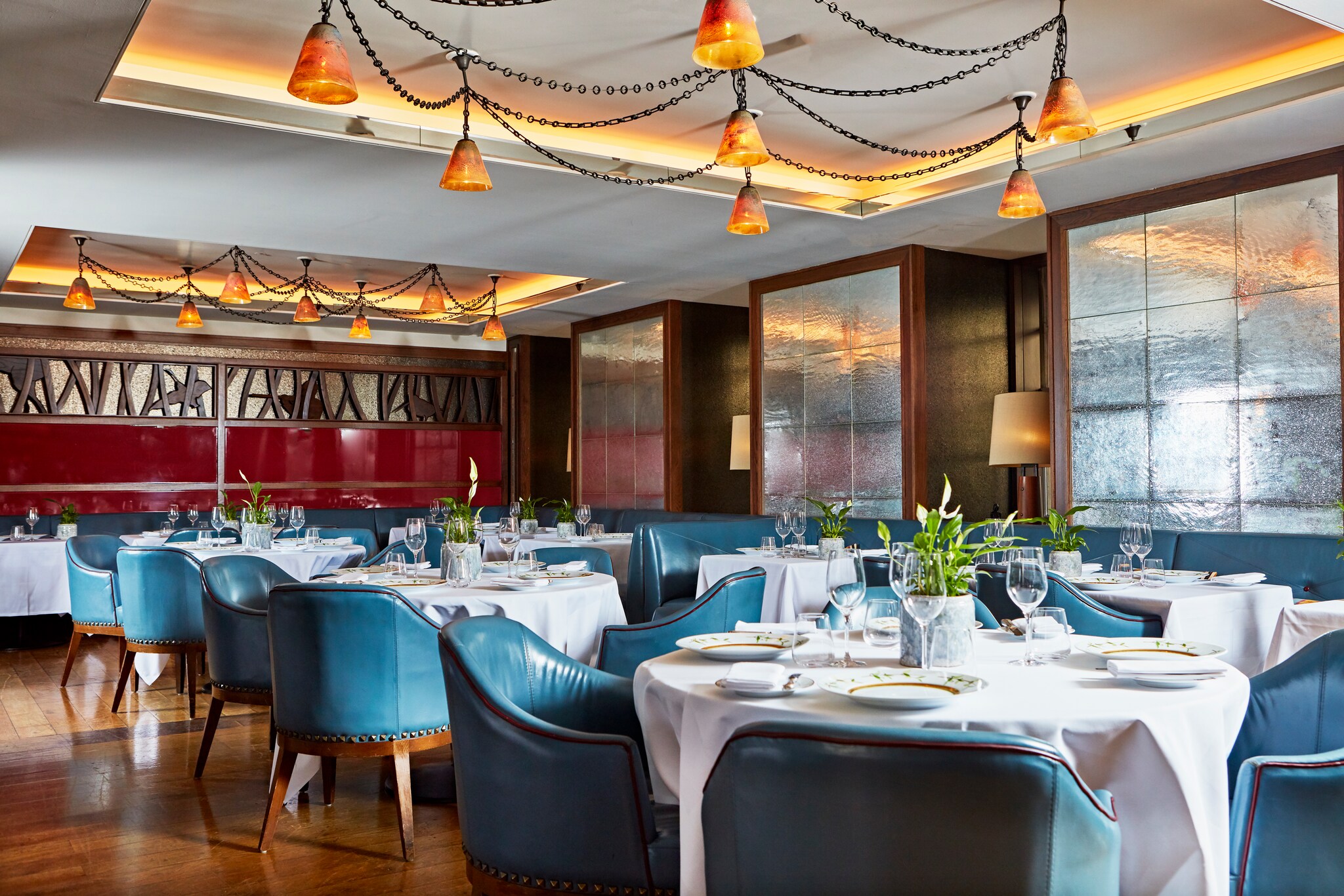 Corrigan’s dining room, with round white tables surrounded by blue leather chairs. Strings of bell-like orange lights hang from the ceiling.