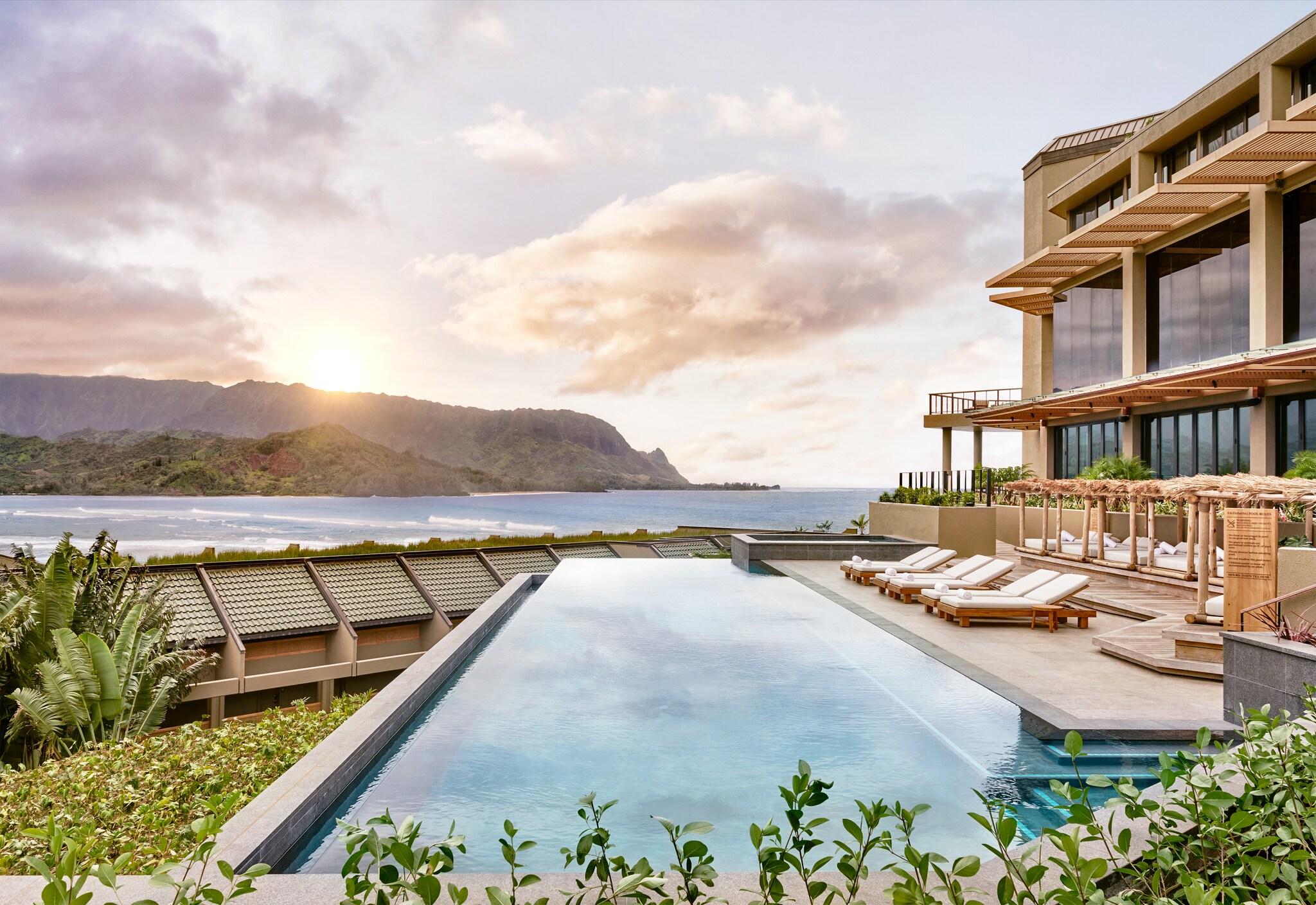 The adult infinity pool at 1 Hotel Hanalei Bay at sunset reflects the changing colors in the sky. Sun beds are set up to overlook the bay.