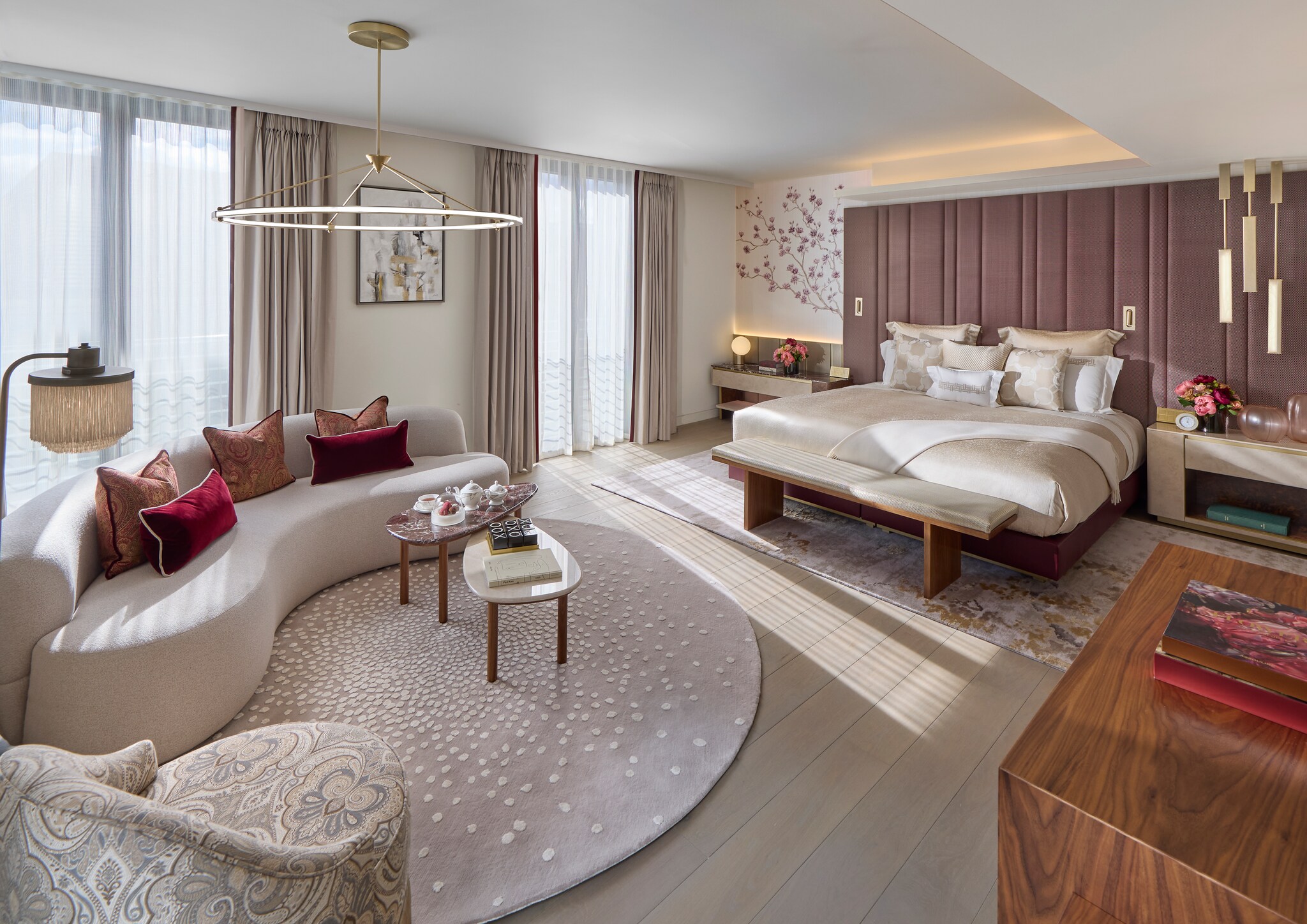 The Mayfair Suite is decorated in cream, gray, and soft rose, with a large bed, floral wall detail, and rug with blossom-like spots.
