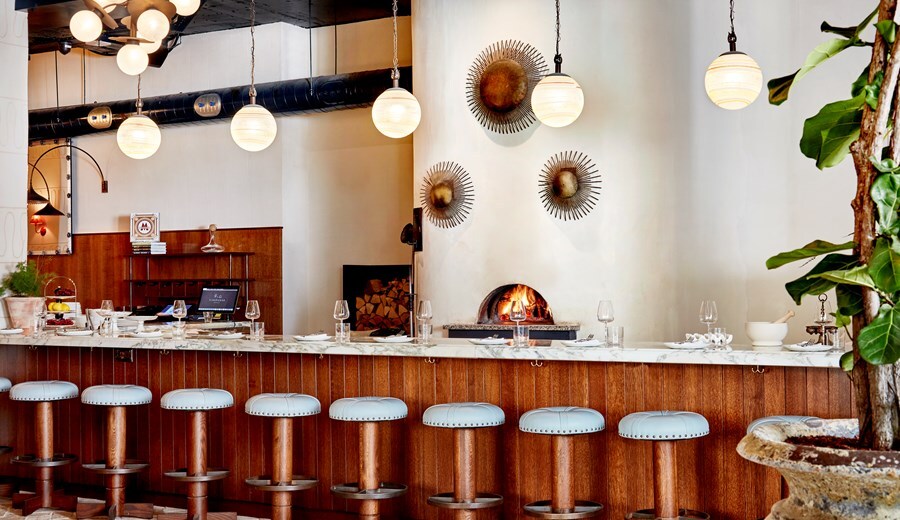 The bar at Pizzeria Mozza is long and brightly lit, with white marble countertops, wooden kick plates, and a line of white-topped stools.
