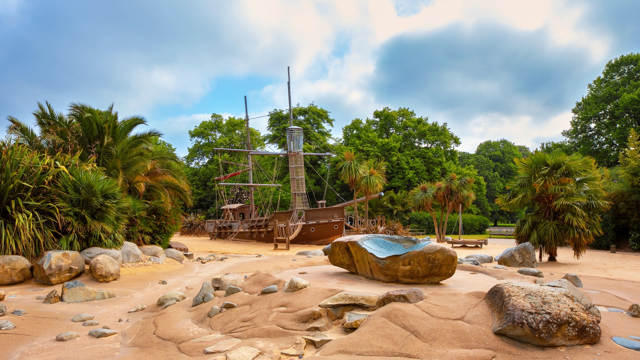The Princess Diana Memorial Playground is lush with palm trees surrounding an island scene with fake sand and a beached pirate ship.