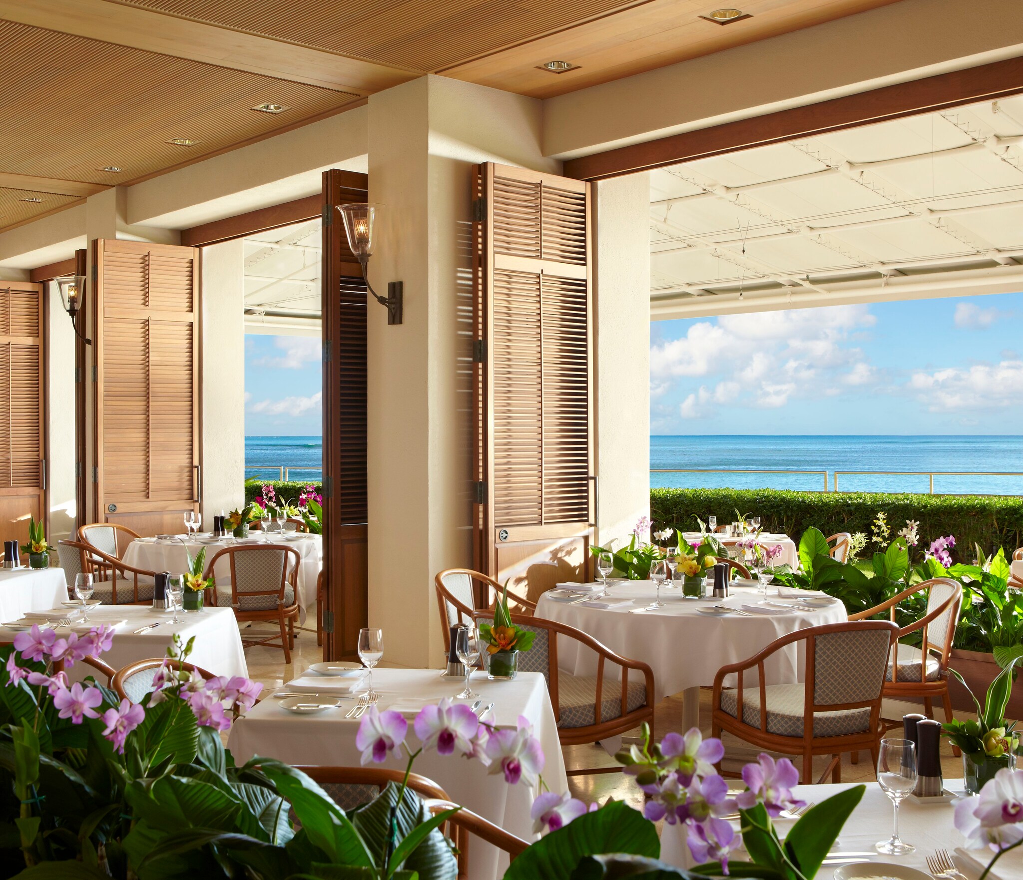 The Orchids restaurant is filled with small tables. Louver doors along one wall open onto lush greenery and the ocean beyond.