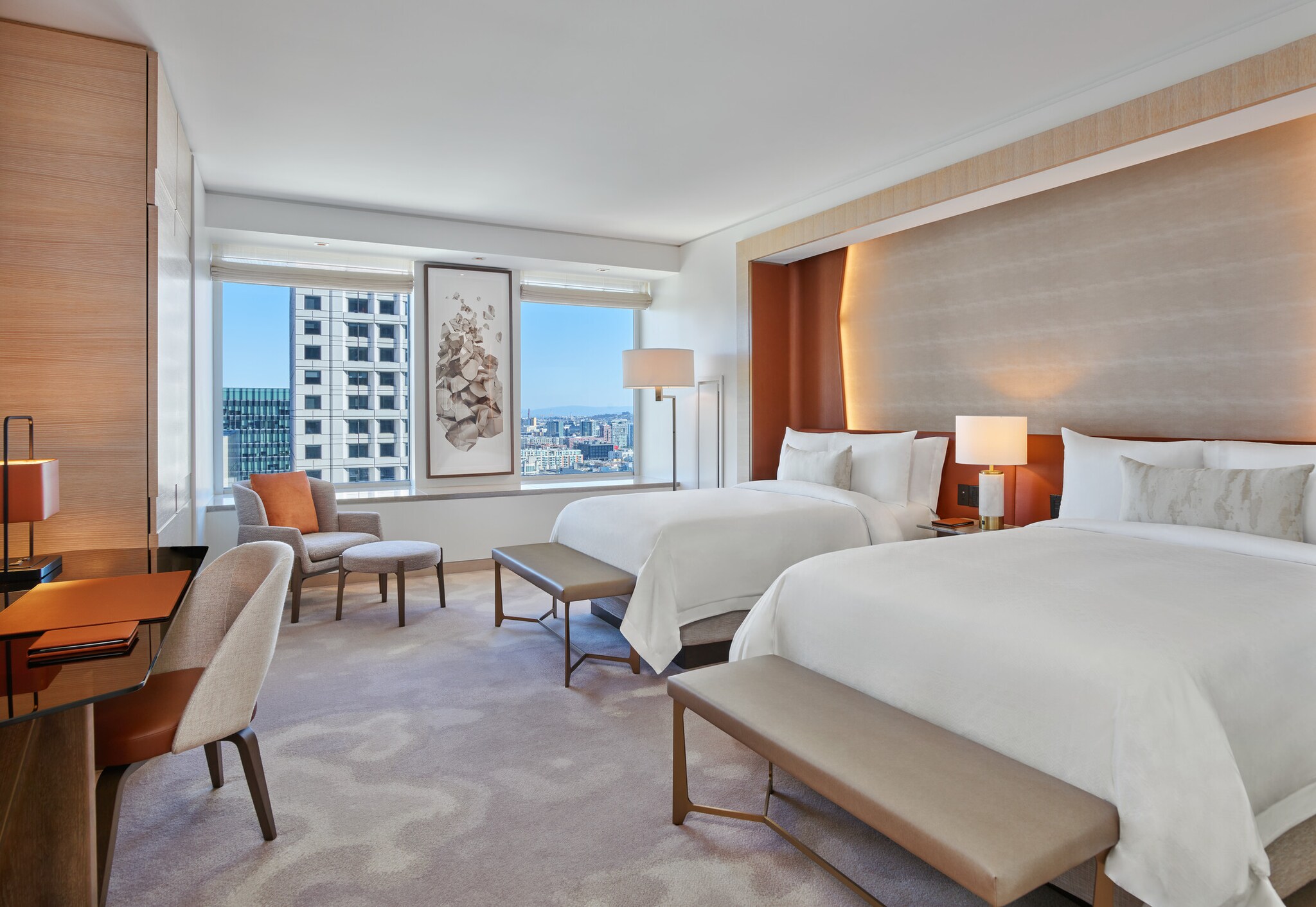 In a double/double grand deluxe guest room at St. Regis San Francisco, on swirled gray carpet, two beds face a trapezoidal black desk.