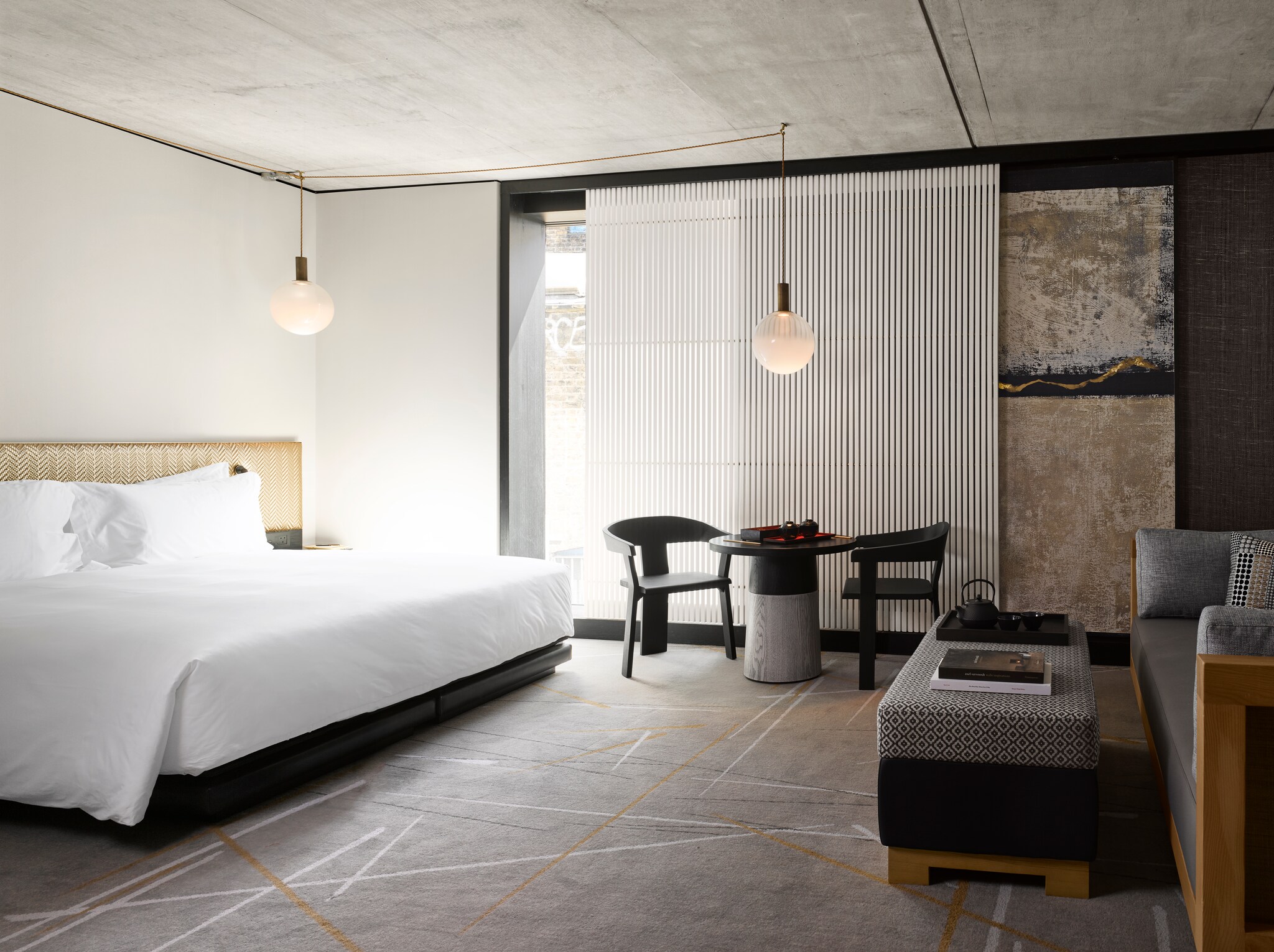 The Nobu Zen Junior Suite is spacious and spare, with a large bed, globular hanging lights, and a slatted curtain in front of a glass door.