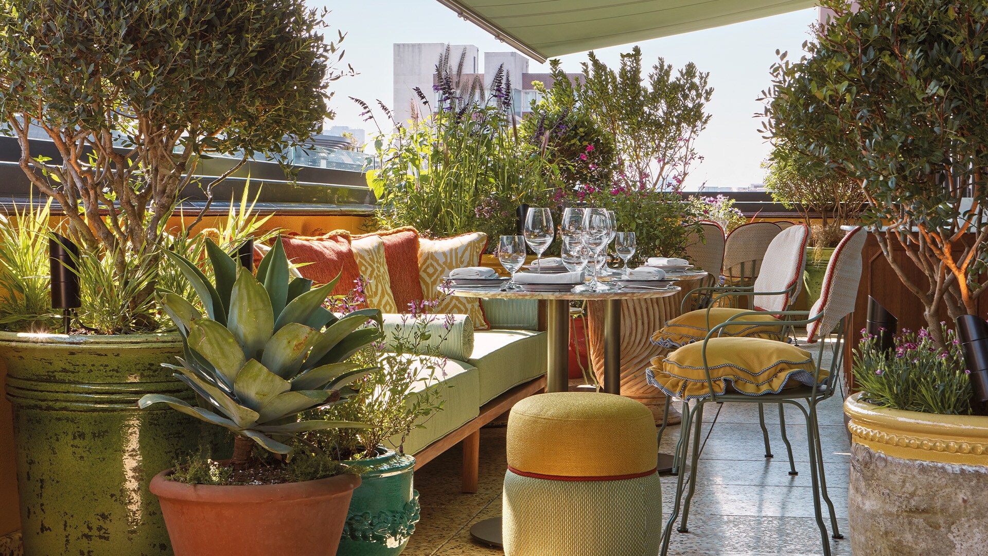 The terrace at the Flute rooftop bar is dense with potted plants against small green tables surrounded by couches and wrought-iron chairs.