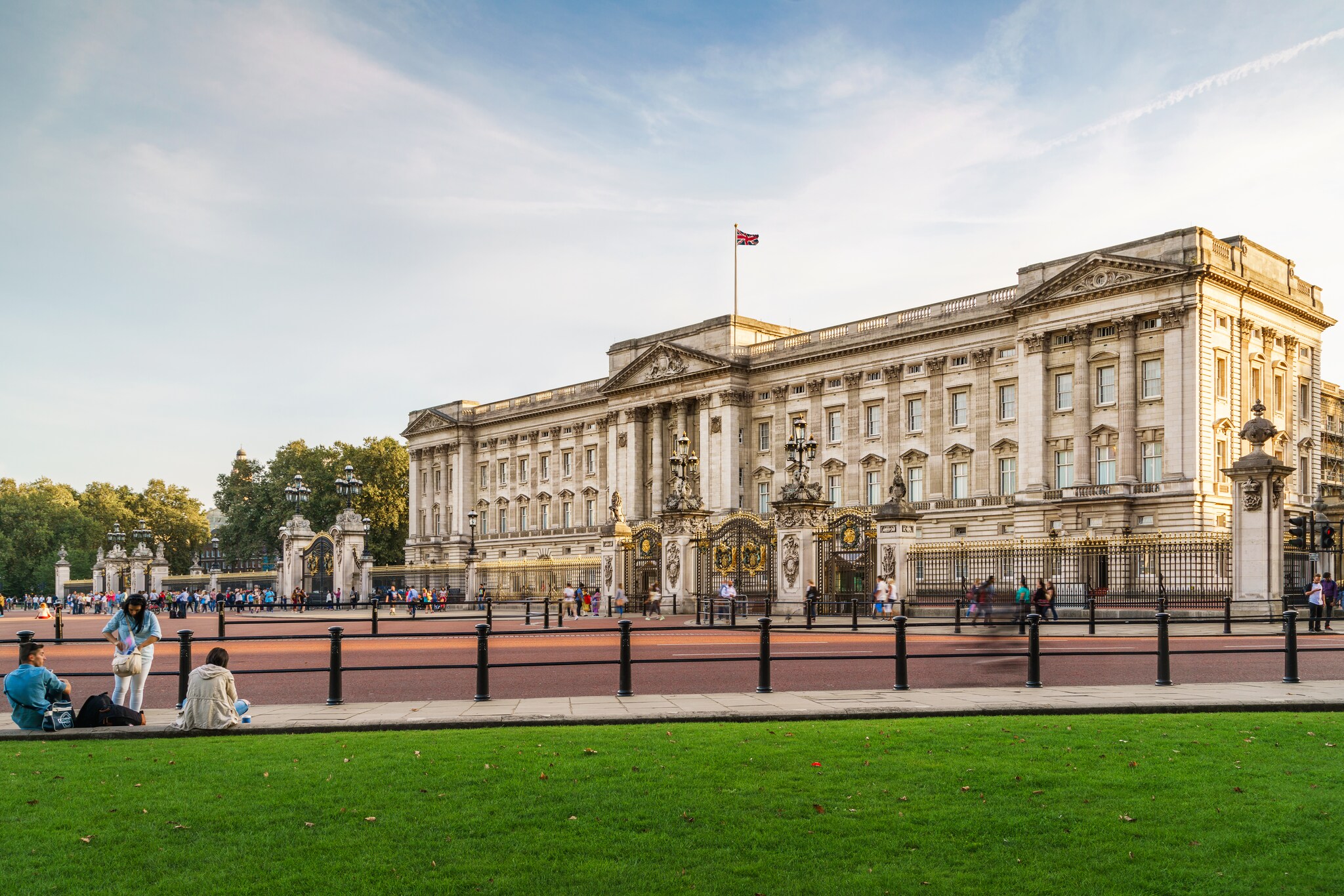 Beyond some grass and the red of Constitution Hill road, Buckingham stands, with a long Neoclassical façade in Belle Époque cream and gold.Beyond some grass and the red of Constitution Hill road, Buckingham stands, with a long Neoclassical façade in Belle Époque cream and gold.