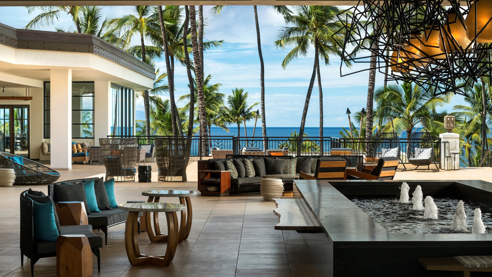 The grand lanai at Wailea Beach Resort features clusters of black and peacock-blue chairs next to a small rectangular fountain.