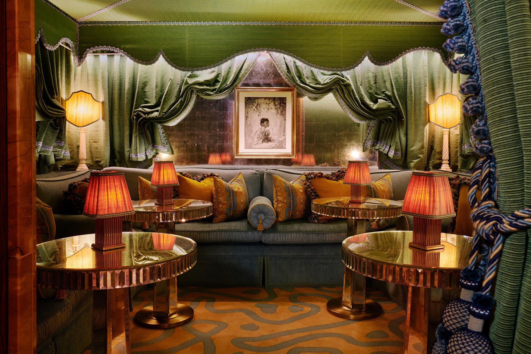  In one of the bars, dense green draperies create a nook around a large green couch and several small, round tables.