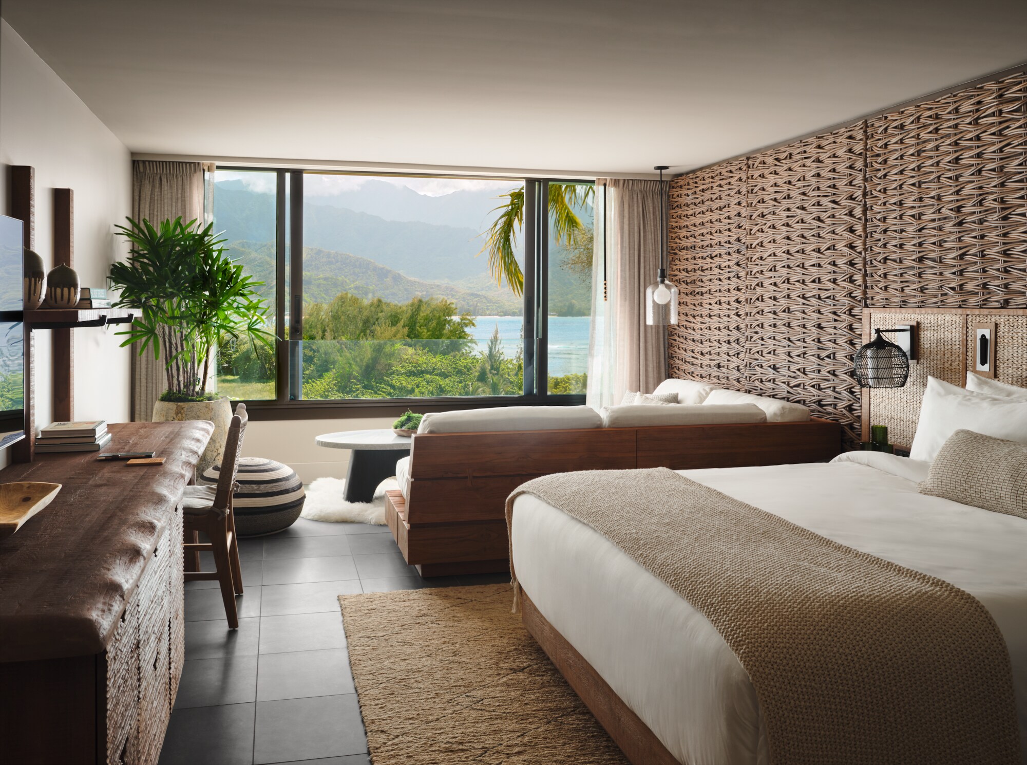 A guest room is decorated in calming whites and browns. One wall is covered in wicker, and a plush white couch faces huge windows.