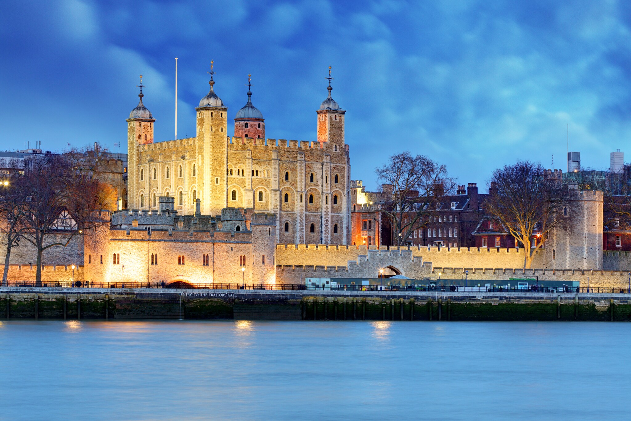 View access the Thames to the Tower of London in the evening, the ramparts and parapets of the castle lit from below.